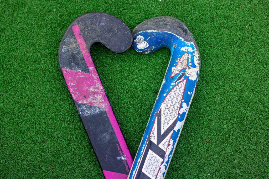 Two field hockey sticks forming a heart shape on green turf.